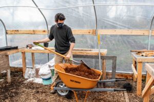 A farmer at 21 Acres shovels compost and other soil amendments in the greenhouse.