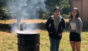 Neha Krishnakumar poses with a friend next to their homemade biochar kiln on the 21 Acres farm.