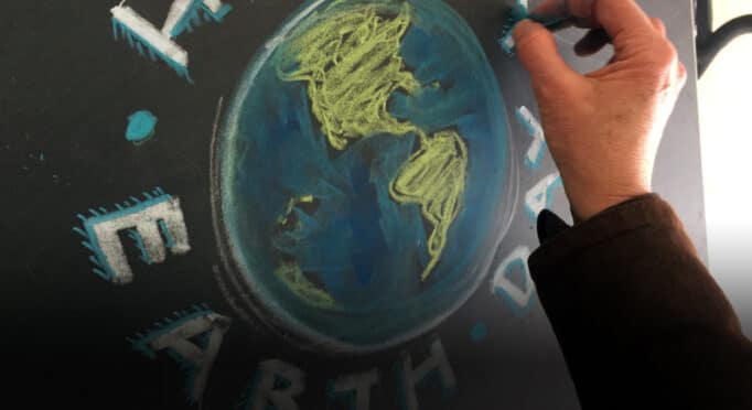 Community member draws Earth Day sign on a chalk board to advocate for issues that matter to them.