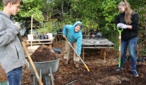 Volunteers shovel mulch into a wheelbarrow on the 21 Acres farm.