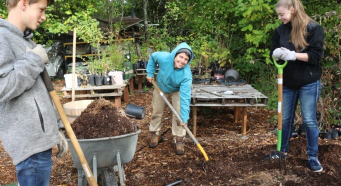 Volunteers shovel mulch into a wheelbarrow on the 21 Acres farm.