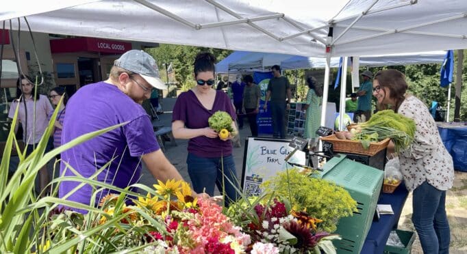 Visitors shop for flowers and produce at the Blue Glass Farm booth on the 21 Acres Farm Market patio.
