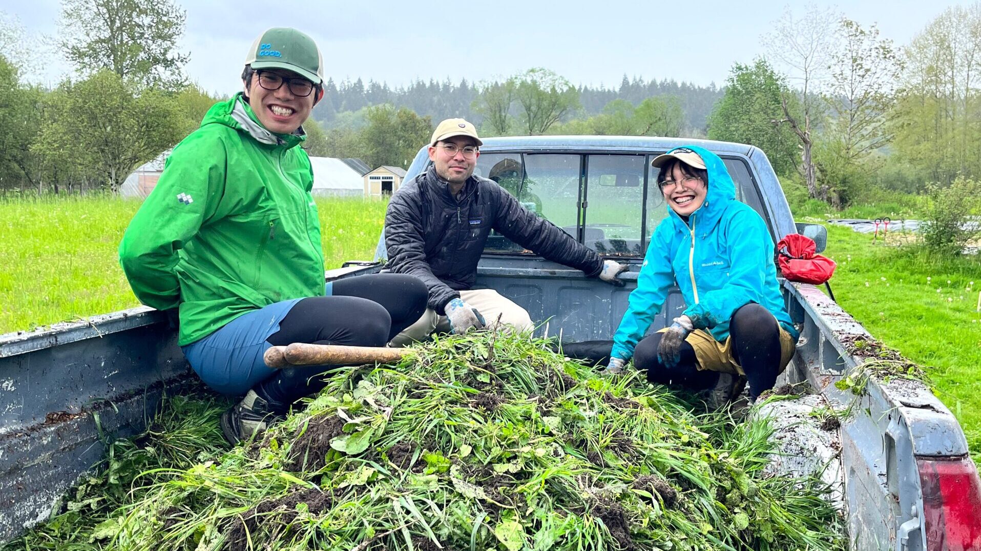 21 Acres volunteers sitting in the bed of a pickup truck loaded with the weeds pulled during a work party.