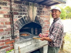 21 Acres volunteer Noah cooks woodfired pizza at the 2023 Volunteer Gratitude Garden Party.