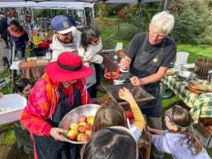 Kids assist Tom Quigley with pressing fresh apple cider at the 2023 Harvest Festival at 21 Acres.